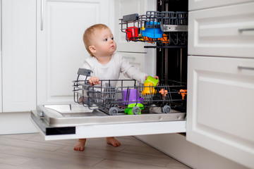 baby loads the dishwasher with plates and his toys. little helper