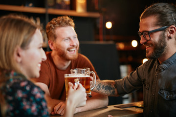 Group of best friends standing at pub and making a toast with beer. Nightlife concept.