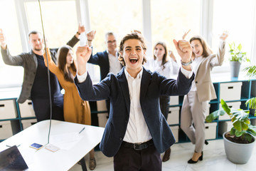 Handsome businessman with win gesture standing in front of his colleagues in office