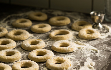 holes in raw homemade doughnuts pastry on the kitchen table covered with flour, preparations for Fat Thursday holiday