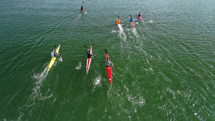 Aerial drone photo of athletes competing in canoe race in tropical lake with emerald waters