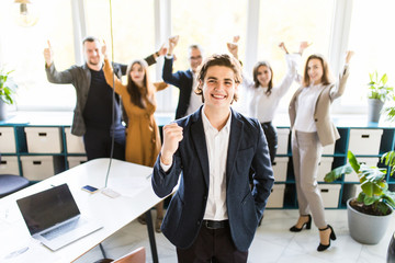 Handsome businessman with win gesture standing in front of his colleagues in office