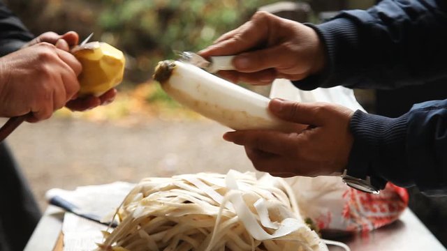 Men peel white daikon radish and potatoes for cooking