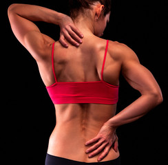 Fototapeta na wymiar Bodybuilder woman suffers from pain in her back and neck after workout, black background