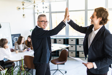 Excited businessman smiling and giving high five to his business partner or colleague while sitting...