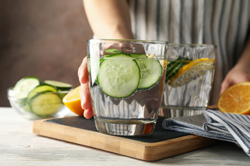 Woman hold glass with cucumber water on white wooden background, close up