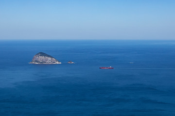 Fototapeta na wymiar Ilha das Cagarras [Shears Island] known as the Whale [Baleia] in the middle of the vast ocean with vibrant blue of the water and light blue sky off the coast of Rio de Janeiro in Brazil