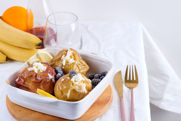 Baked apples with blueberries and cottage cheese in bowl with cutlery on white table