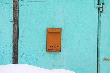 Old orange mailbox attached to a turquoise cracked wall.