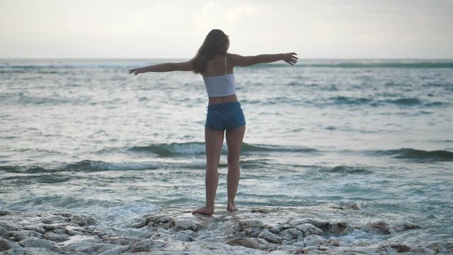 A girl on the ocean raises her hands up, admires the waves. 4k