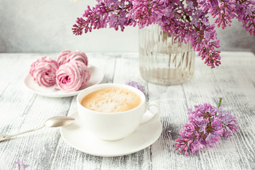 Fototapeta na wymiar Cup of coffee, homemade marshmallow, lilac flowers. Romantic spring morning Selective focus