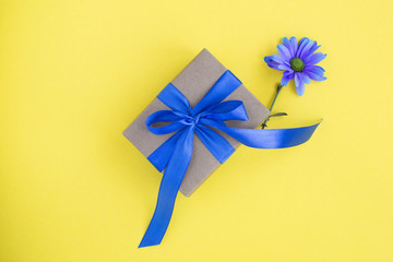Gift with blue bow and  one blue flower in the center of  the yellow background. Top view. Copy space.