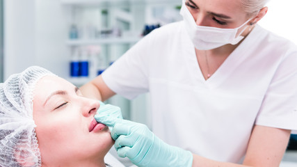 The young beautician doctor preparing to making injection in female lips. The doctor cosmetologist...