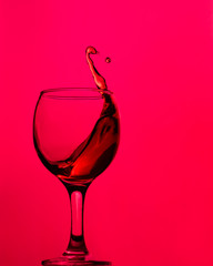Splash of wine in a glass on a red background. Monochrome