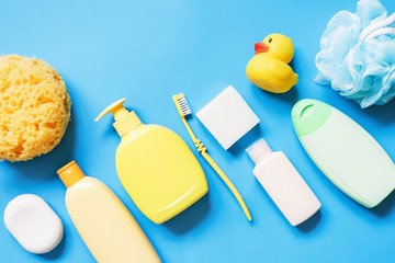 Yellow sponge, soap bar, shampoo bottle, toothbrush, shower gel, hair balm and rubber duck on a blue background. Flat lay photography bath products, baby care cosmetic