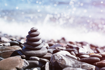 Stone pebble tower balancing on the beach with sparkling sea waters splash bokeh. Copy space. Balance and mindfulness.