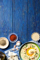 Fototapeta na wymiar Chickpea hummus and various ingredients on a dark blue wooden background