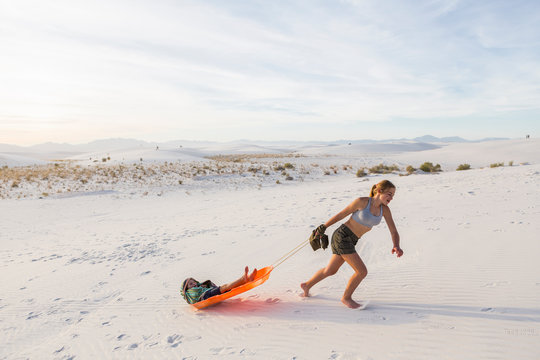 13 Year Old Girl Pulling Her Brother In Sled At Sunset, White Sands Nat'l Monument, NM,White Sands National Monument