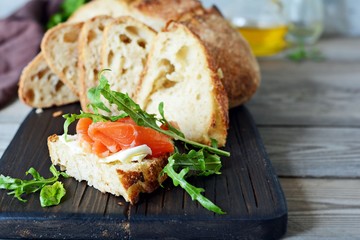 Sandwich with slightly salted salmon, arugula, seeds and cottage cheese on the board. Sourdough bread toast with salted fish, smorrebrod.