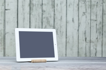 The tablet is on the table on the background of wooden boards.