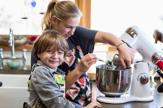 Thirteen year old teenage girl and her 6 year od brother in the kitchen,using a mixing bowl