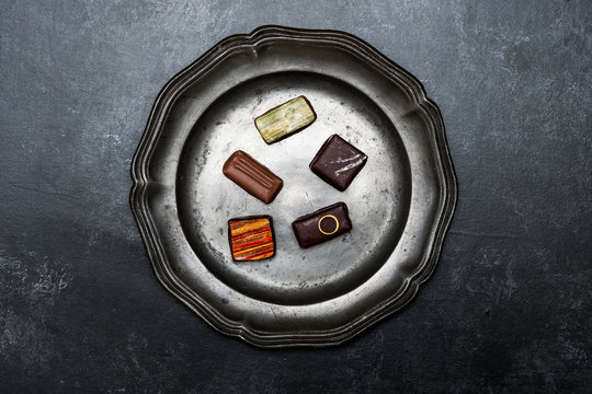 High angle close up of a selection of chocolate pralines on a tin plate on black background.