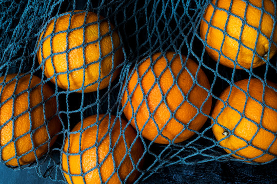 High angle close up of oranges in grey net bag on black background.