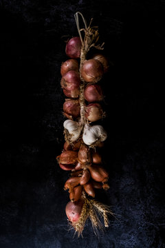 High angle close up of string of onions and garlic on black background.