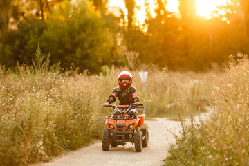 The little girl rides a quad bike ATV. A mini quad bike is a cool girl in a helmet and protective clothing. Electric quad bike electric car for children popularizes green technology. © Angelov