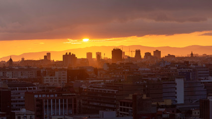 Sunset over the skyline of Barcelona. Silhouettes of buildings in the orange rays of the sun.