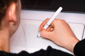 Female hands work on a graphic tablet. Hand holds stylus pen and draws. White graphic tablet. The...