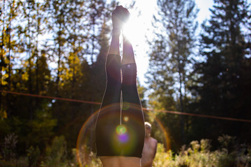 A closeup view on the legs and feet of a woman standing upside down, headstand with backlight and lens flare in woodland during mindful yoga in nature. Soft focus shot