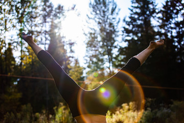 A close up shot on the legs of a woman doing a handstand in nature with low afternoon sun and colorful lens flare, blurry forest trees in background