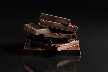 Broken chocolate pieces on a black background. Copy space. Close-up.