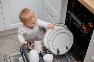 baby loads the dishwasher with plates and his toys. little helper