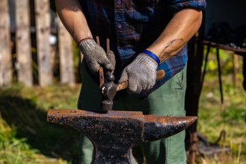 A close up view of a man using a hammer, to work hot metal on a blacksmith anvil during a demonstration at a festival celebrating cultural creatives