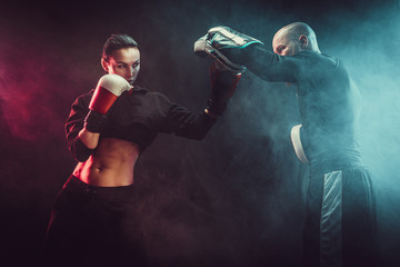 Woman exercising with trainer at boxing and self defense lesson, studio, smoke on background.