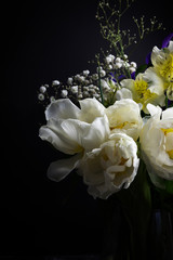 Flowers in a vase on a black background tulips, alstromeria, irises