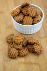 Very tasty peanut butter biscuits on bamboo wooden board in white baking bowl, golden baked healthy cookies