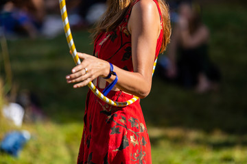 A side profile midsection view in soft focus of a healthy woman with bronzed skin and red dress, exercising with a hula hoop at festival campsite © Valmedia