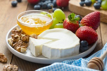 Cheese plate round sliced soft cheese, blueberry, strawberry, grapes and honey on wooden table.