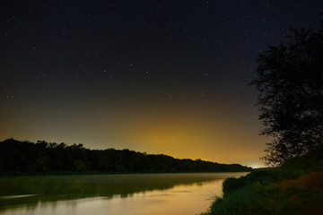 Milky Way stars in the sky above the river. Night landscape photographed with a long exposure.