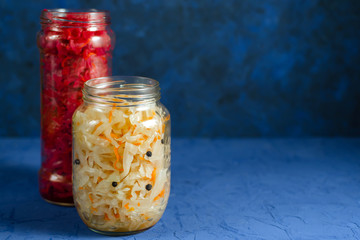 fermented pickled vegetables in various modern glass jars, ready for closing. white with pepper and red with beetroot cabbage on a classic blue background with place for text