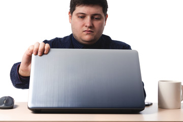 A young guy in a dark blue shirt opens a laptop next to an office, business cup of coffee on a white background. isolate. copy space