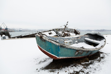 Old broken lifeboat lies on a pier in winter