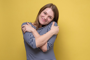 Relaxed happy young woman hugging herself, having pleased joyful facial expression.