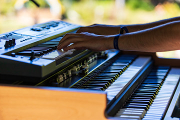 A close up and side profile view of a modern musician using a three tier electronic keyboard and synthesizer during a multicultural festival. Soft focus