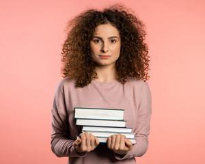 European student on pink background in studio holds stack of university books from library. Woman is happy to graduate.