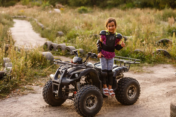 The little girl rides a quad bike ATV. A mini quad bike is a cool girl in a helmet and protective clothing. Electric quad bike electric car for children popularizes green technology.