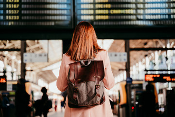 young woman at train station looking at destination board. Travel and public transport concept